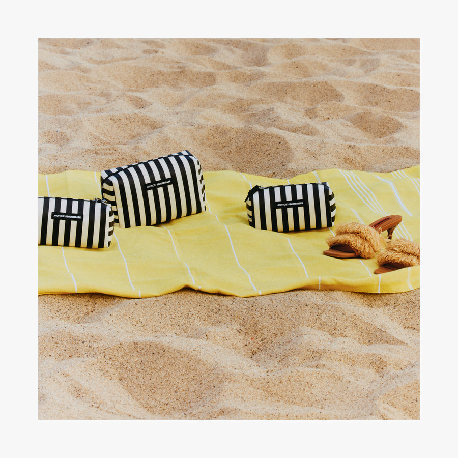 Small / Poplin Stripe Black | Three Metro Toiletry Cases in Poplin Stripe Black arranged on a yellow towel laid out on sandy beach